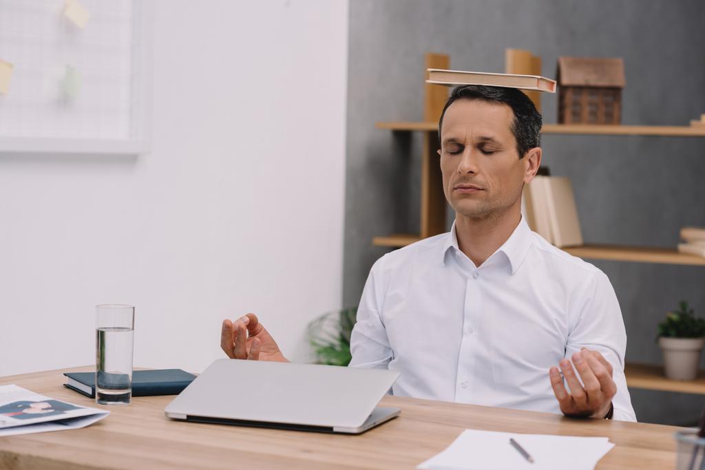 спокойный бизнесмен медитирует с книгой на голове в офисе
 - Фото, изображение