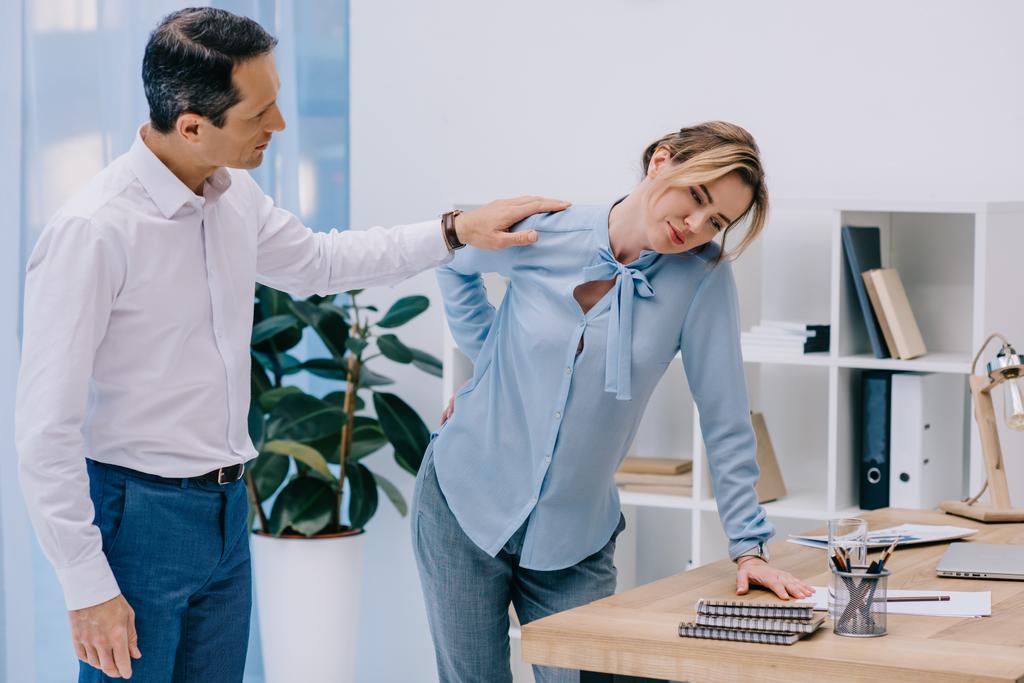attractive businesswoman has back pain while her colleague trying to help her at office - Photo, Image