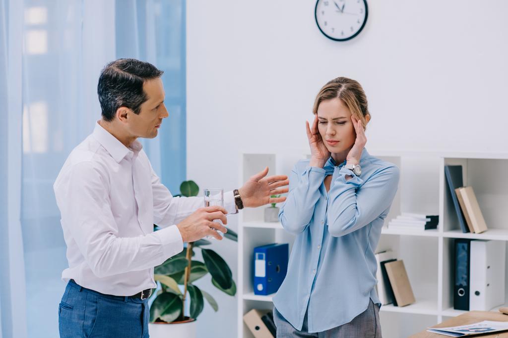 aantrekkelijke zakenvrouw heeft hoofdpijn terwijl haar collega probeert haar te helpen op kantoor - Foto, afbeelding