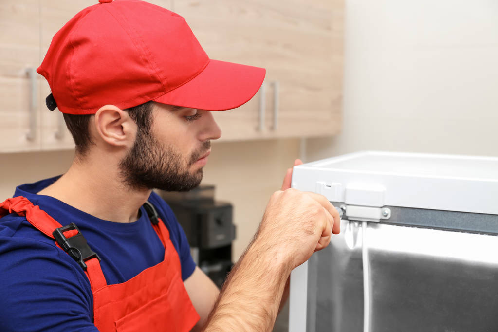 Чоловічий технік ремонтує холодильник в приміщенні
 - Фото, зображення