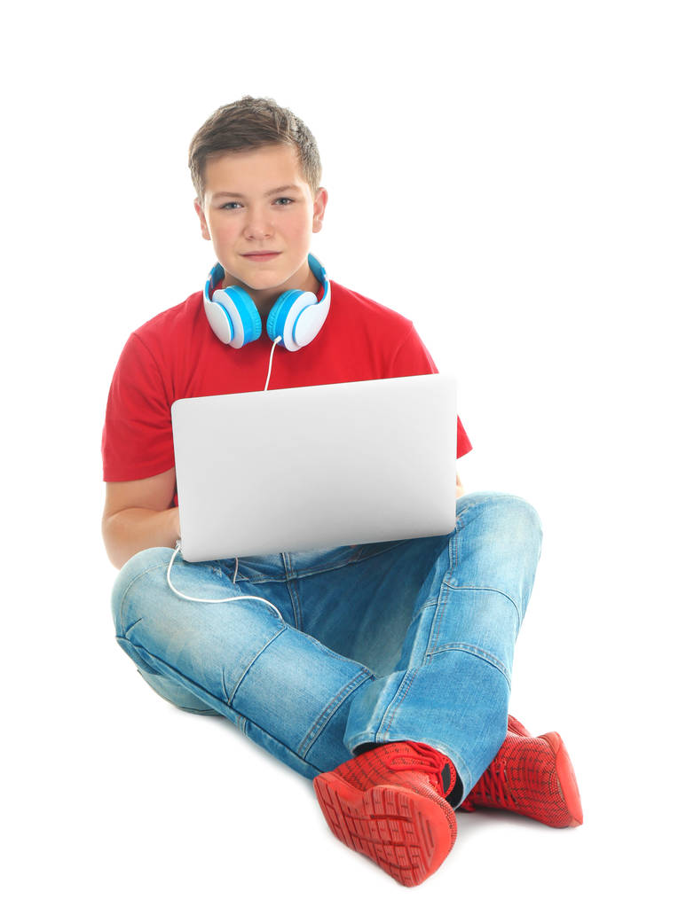 Εφηβικό αγόρι με φορητό υπολογιστή και ακουστικά σε λευκό φόντο - Φωτογραφία, εικόνα