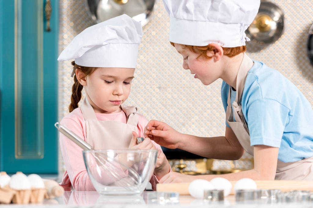 bellissimi bambini in cuoco cappelli e grembiuli che cucinano insieme in cucina
 - Foto, immagini