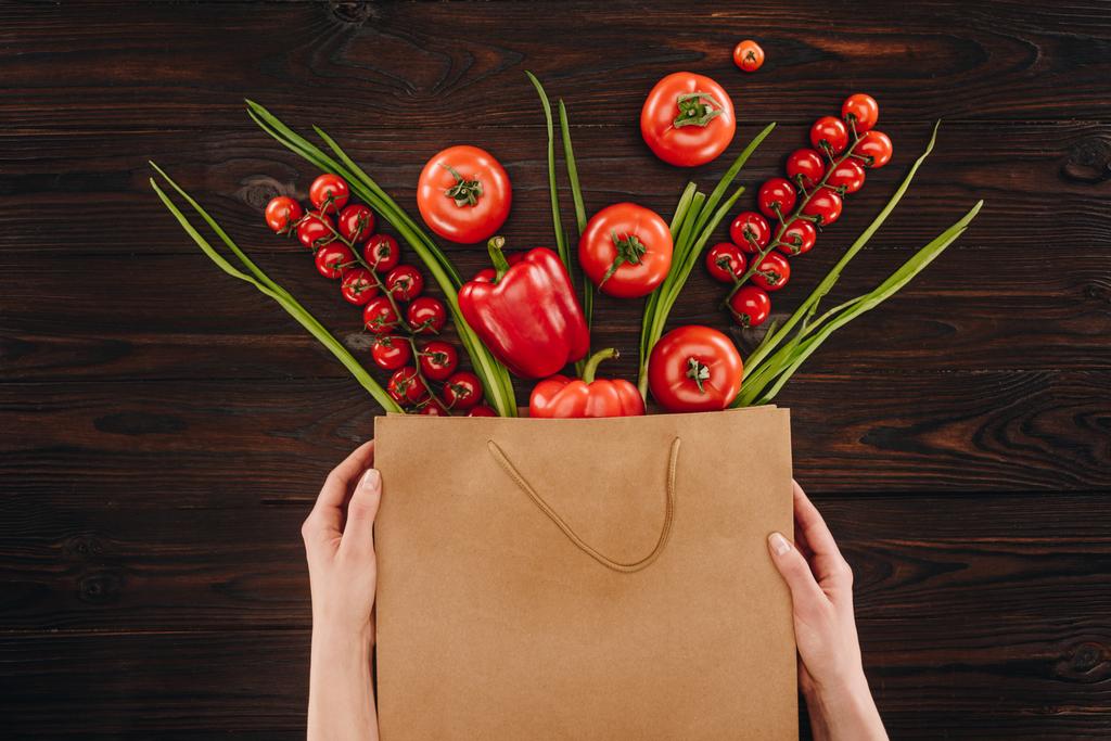 обрезанное изображение девушки, держащей сумку с овощами на деревянном столе
 - Фото, изображение
