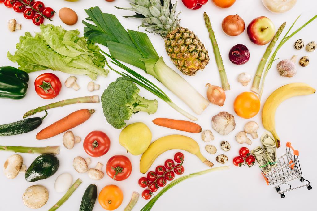 vista superior del pequeño carrito de compras con dólares y frutas con verduras aisladas en blanco
 - Foto, Imagen