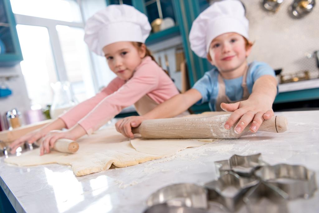 lindo niños pequeños preparando la masa y sonriendo a la cámara en la cocina
 - Foto, imagen