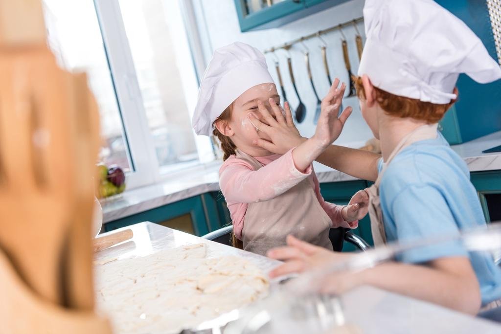 επιλεκτική εστίαση του αξιολάτρευτο μικρό παιδιά σε καπέλα σεφ διασκεδάζοντας με αλεύρι στην κουζίνα - Φωτογραφία, εικόνα
