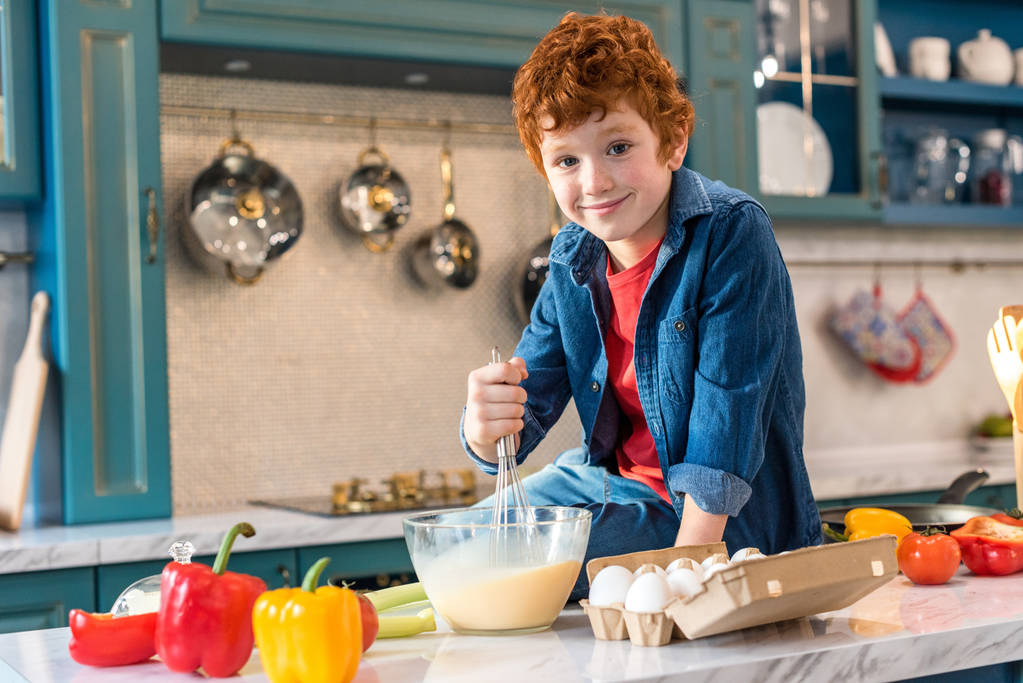milý chlapeček se usmívá na kameru při vaření v kuchyni - Fotografie, Obrázek