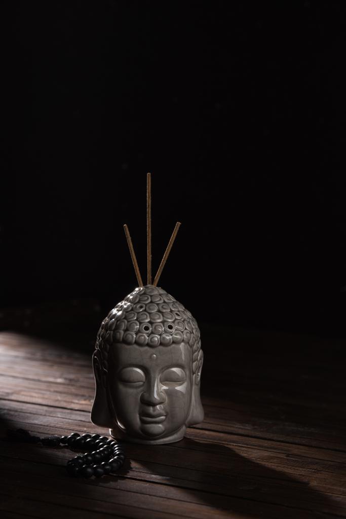 Skulptur eines Buddhakopfes mit Räucherstäbchen auf Holztisch - Foto, Bild