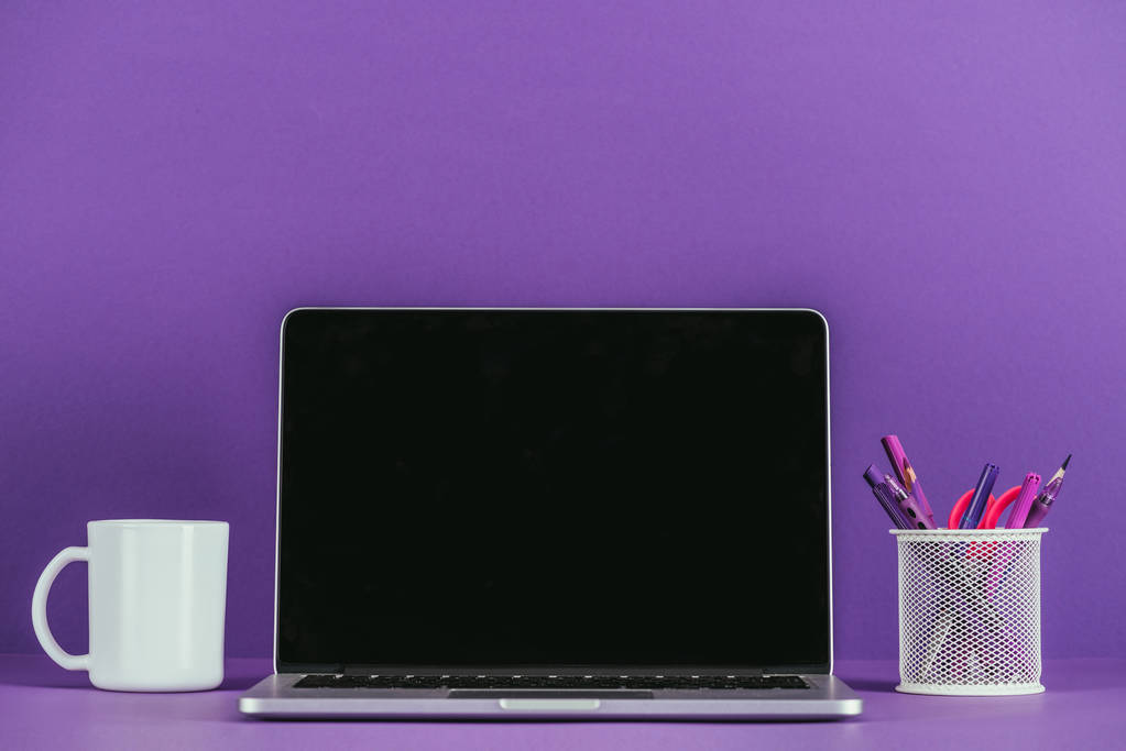 Arbeitsplatz mit Laptop und Kaffeebecher auf violetter Oberfläche - Foto, Bild