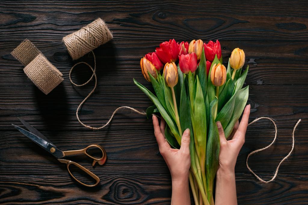 visão parcial das mãos femininas, corda, tesoura e buquê de flores na superfície de madeira
 - Foto, Imagem