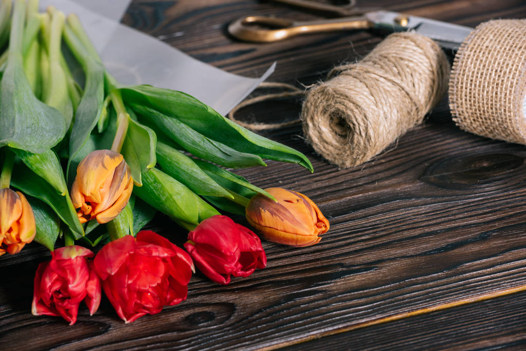 Nahaufnahme eines Straußes aus Tulpen, Schleife, Schere und Seil auf einer hölzernen Tischplatte - Foto, Bild