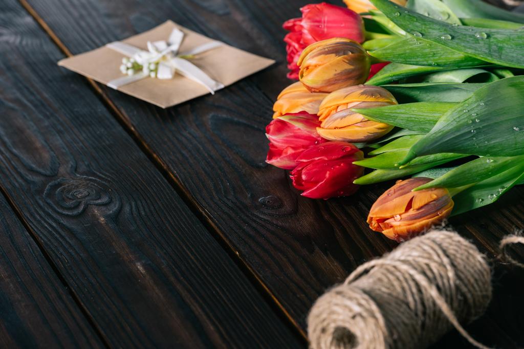close up view of bouquet of tulips, postcard and rope on wooden tabletop - Photo, Image
