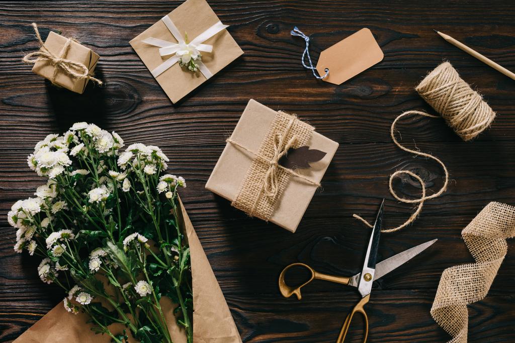 плоский укладка с обернутыми подарками, букет цветов, веревка и ножницы на деревянной поверхности
 - Фото, изображение