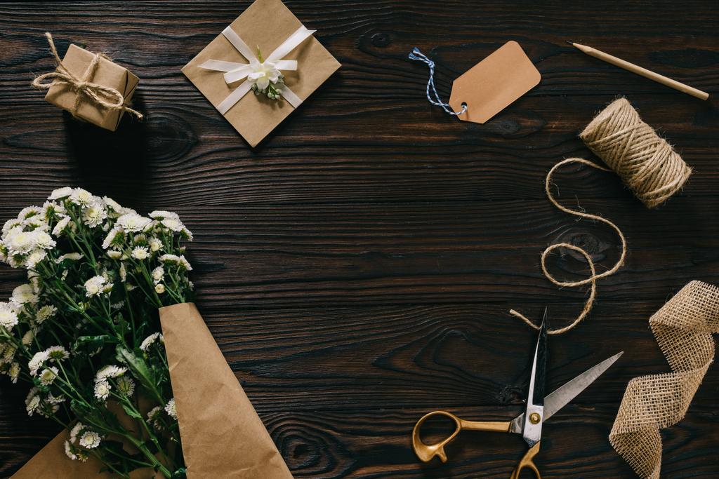 flache Liege mit eingewickeltem Geschenk, Blumenstrauß, Seil und Schere auf Holzoberfläche - Foto, Bild