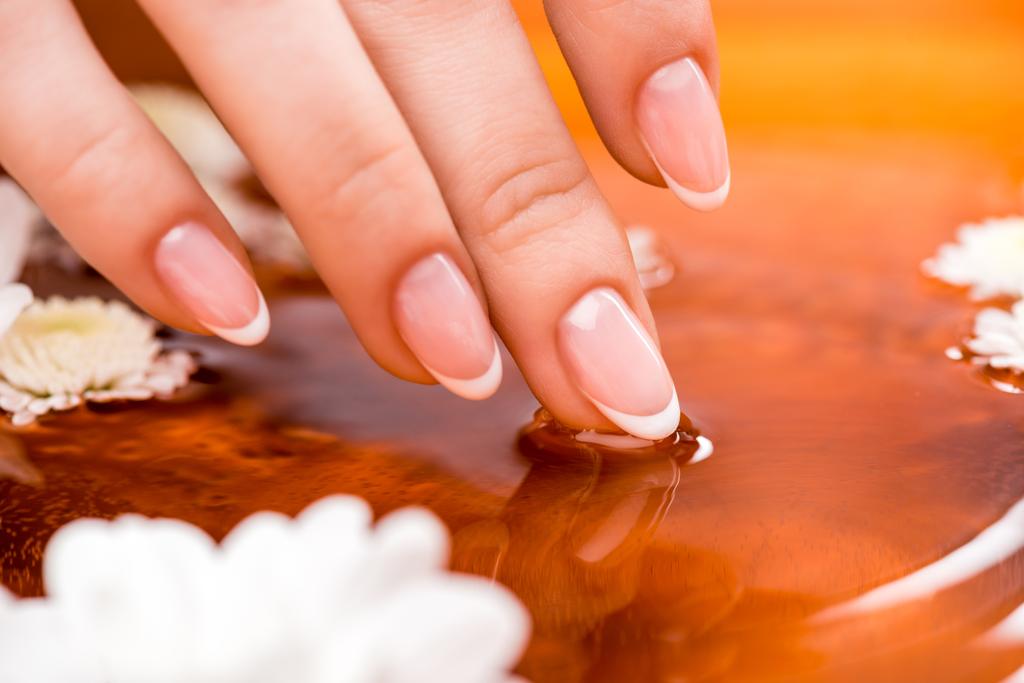обрезанный вид женщины, принимающей ванну с цветами для ногтей
 - Фото, изображение