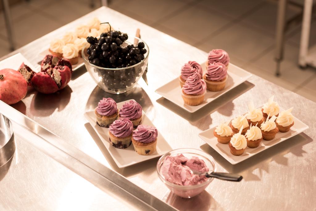 κοντινό πλάνο προβολής των σταφυλιών, κρέμα και γλυκό κέικ στα πιάτα στον πάγκο σε κουζίνα εστιατορίου - Φωτογραφία, εικόνα