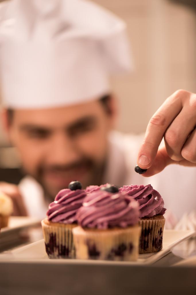 επιλεκτική εστίαση του ζαχαροπλάστη διακόσμηση cupcakes με μούρα σε κουζίνα εστιατορίου - Φωτογραφία, εικόνα