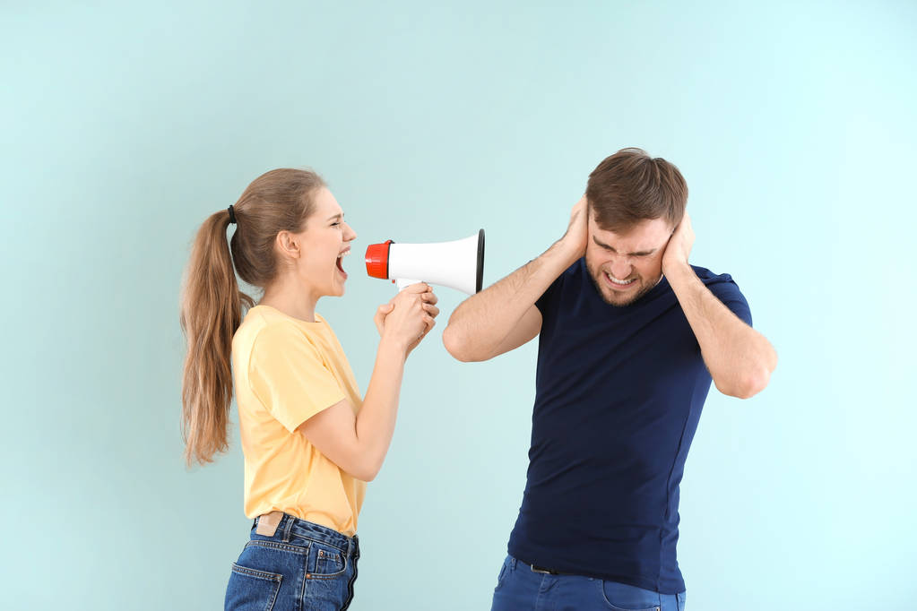 Mujer joven gritando en megáfono al hombre en el fondo de color. Problemas en la relación
 - Foto, Imagen