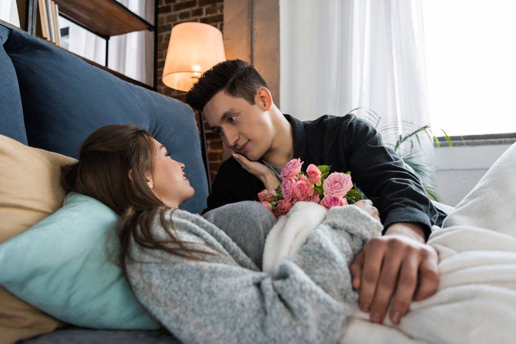 namorado apresentando buquê de rosas para namorada na cama no dia internacional das mulheres
 - Foto, Imagem