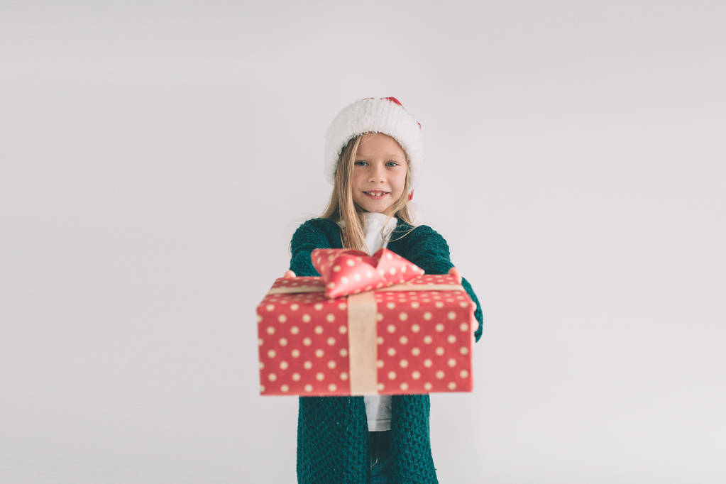 Petite fille dans un chapeau de Noël tenant des cadeaux sur fond blanc. Nous vous souhaitons un joyeux Noël et une bonne année
. - Photo, image