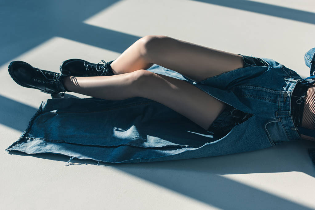 vista ritagliata di ragazza in abiti di jeans sdraiato sul pavimento con ombre
 - Foto, immagini