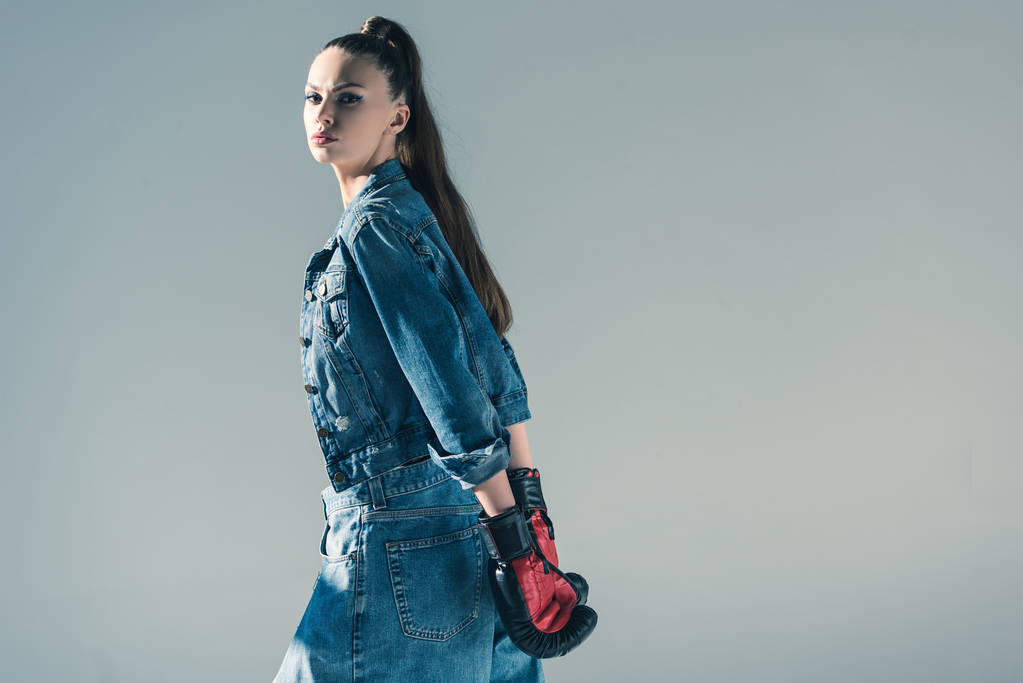 stylisches brünettes Mädchen in Jeans und Boxhandschuhen, isoliert auf grau - Foto, Bild