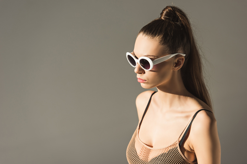 модна брюнетка дівчина з зачіскою з хвоста в сонцезахисних окулярах, ізольована на сірому
 - Фото, зображення