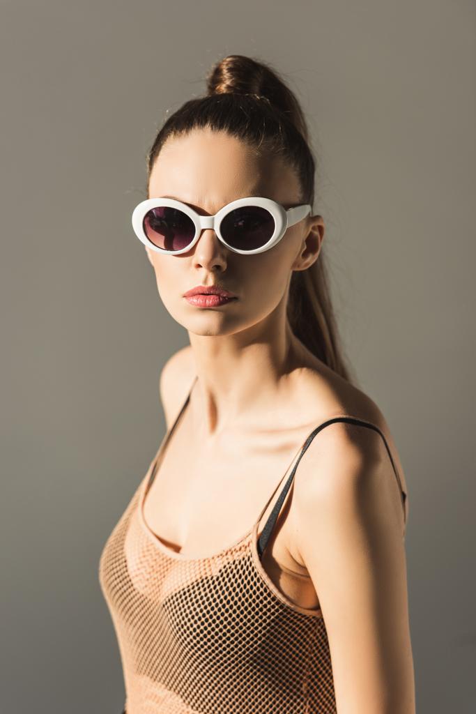 стильная девушка в солнцезащитных очках с хвостиком, изолированная на сером
 - Фото, изображение