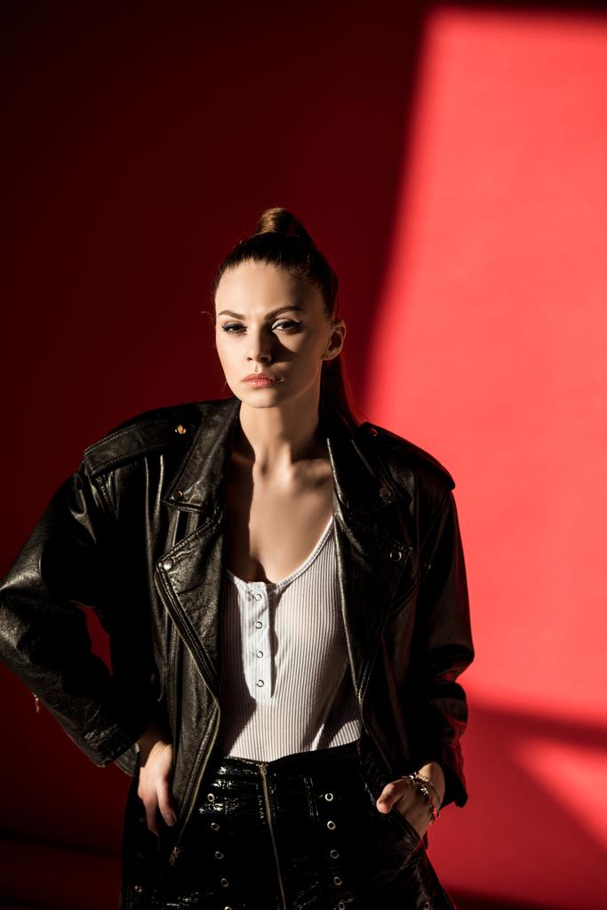 attractive young woman posing in black leather jacket for fashion shoot on red - Photo, Image