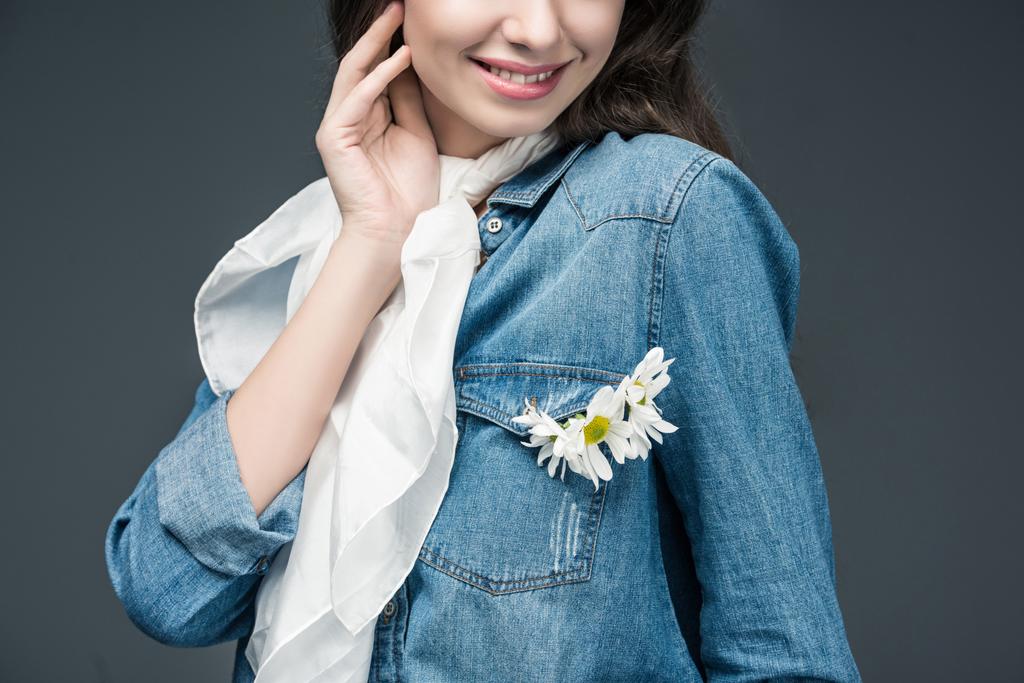 abgeschnittene Ansicht eines lächelnden Mädchens in Schal und Jeanshemd mit Blumen, isoliert auf grau - Foto, Bild