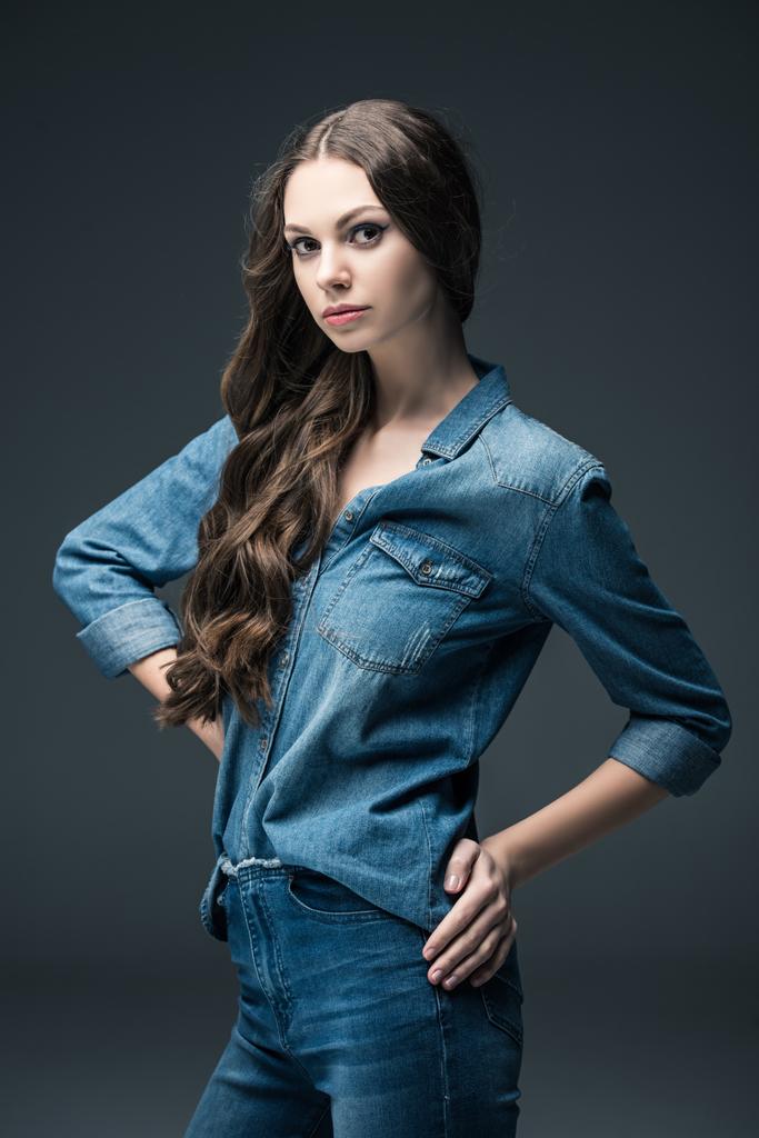 hübsches Mädchen mit langen brünetten Haaren posiert in Jeanskleidung, isoliert auf grau - Foto, Bild