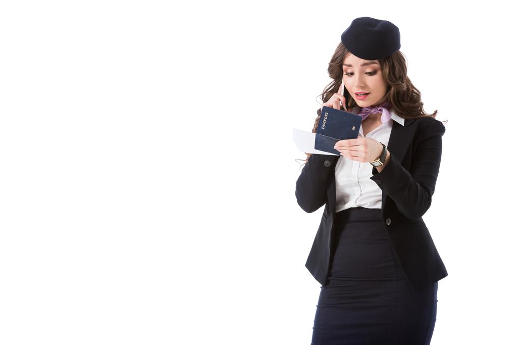 atraktivní letuškou mluví o smartphone a při pohledu na letenky a pas izolované na bílém - Fotografie, Obrázek