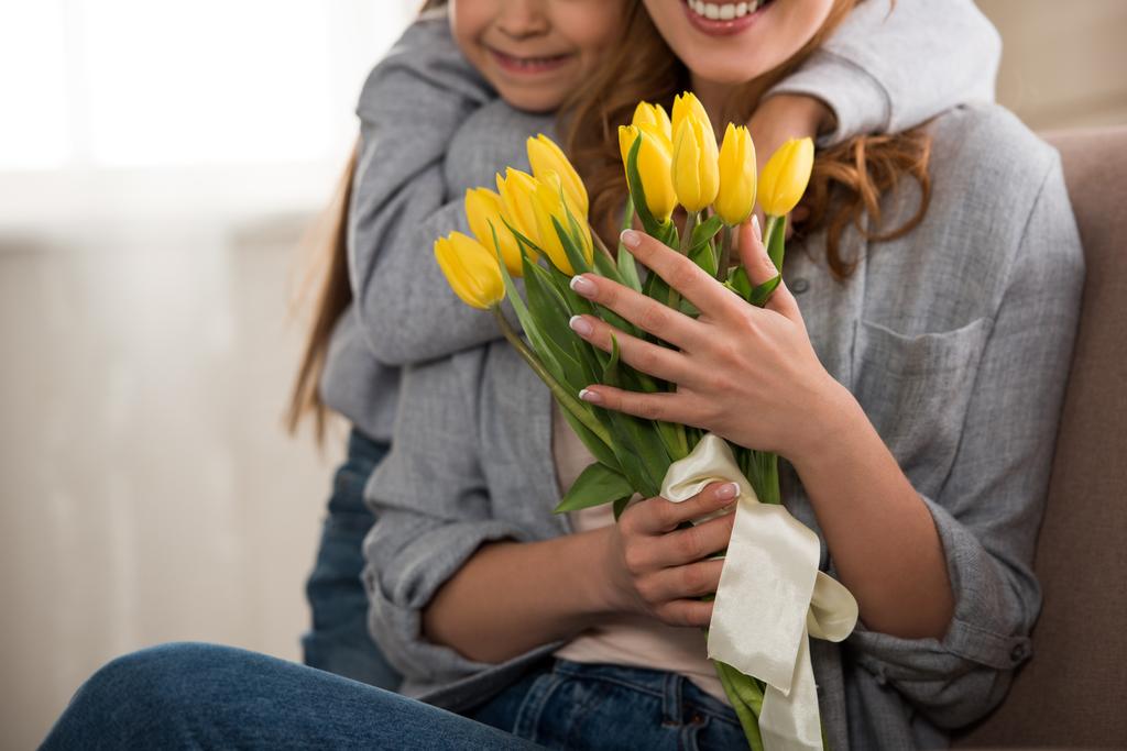 обрезанный снимок счастливого ребенка, обнимающего улыбающуюся мать с желтыми тюльпанами
 - Фото, изображение