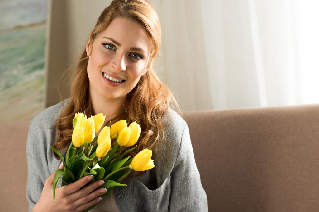 приваблива молода жінка тримає жовті тюльпани і посміхається на камеру
  - Фото, зображення