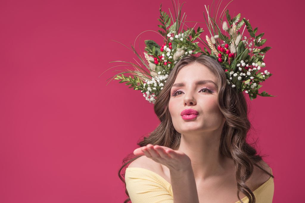 beautiful girl with flowers and herbs wreath on head sending air kiss isolated on burgundy - Photo, Image