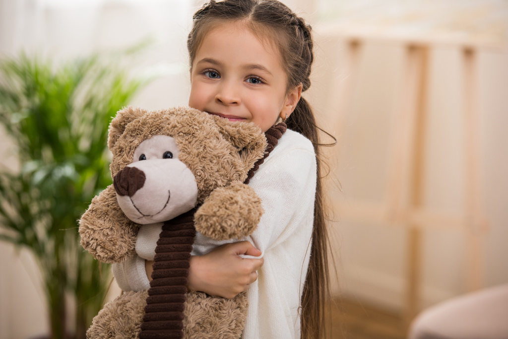 Imádnivaló kis gyermek teddy medve átölelve és mosolyogva kamera - Fotó, kép