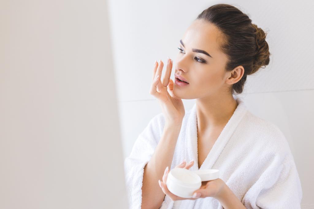 portrait of beautiful woman in bathrobe applying face cream - Photo, Image