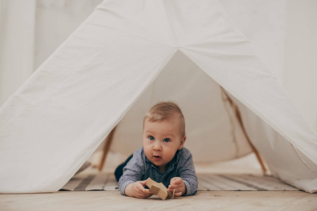 Porträt eines Jungen, der mit Spielzeug auf Holzboden im Zelt liegt - Foto, Bild