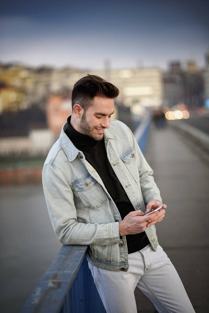 Jonge knappe man met zijn mobiele telefoon, genieten van een dag op straat - Foto, afbeelding