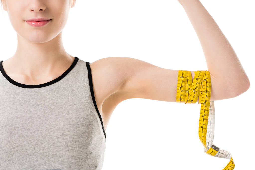 cropped shot of young woman showing her biceps tied with measuring tape isolated on white - Photo, Image
