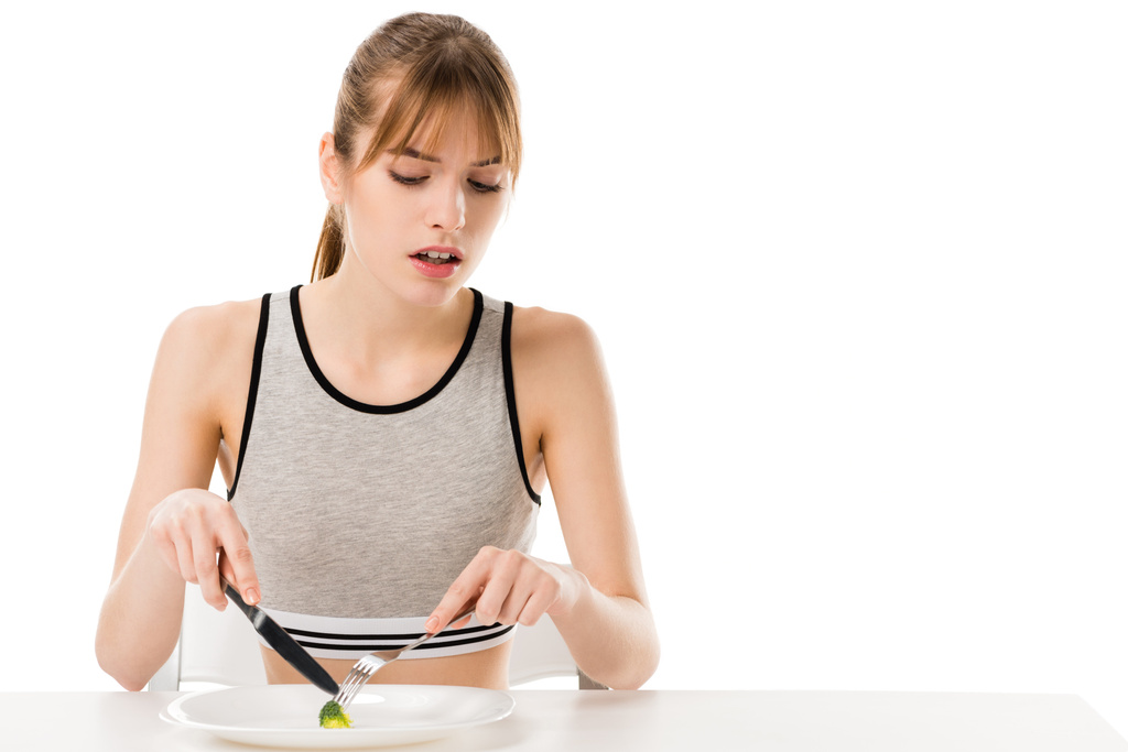 walgt slanke vrouw eten van stukje broccoli van geïsoleerd op een witte plaat - Foto, afbeelding