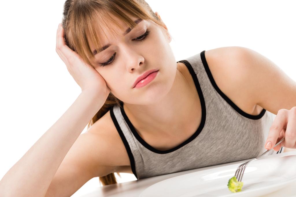 surullinen ohut nainen syö pala parsakaalia lautaselta eristetty valkoinen
 - Valokuva, kuva