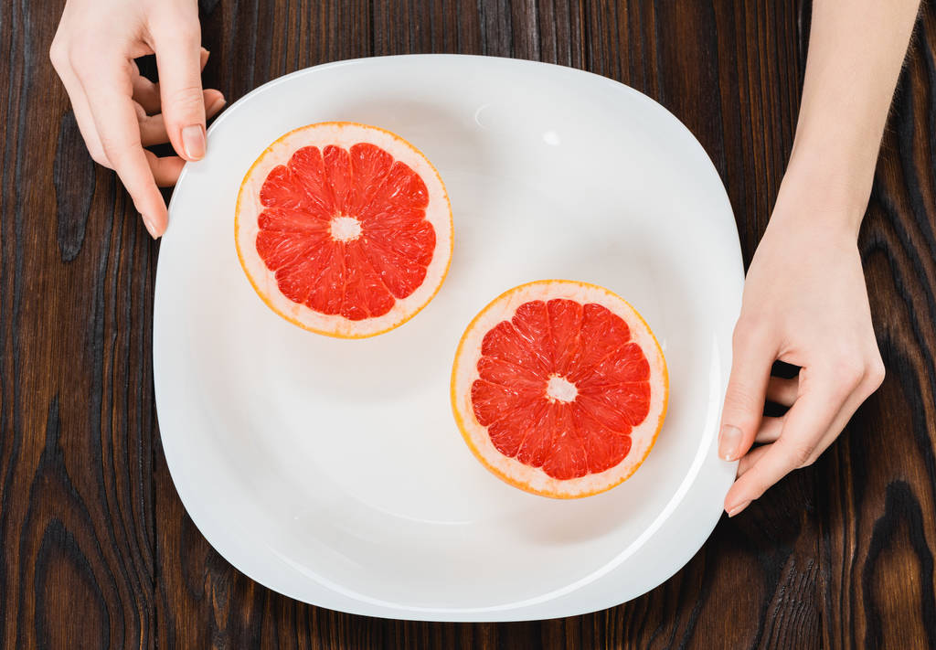 обрезанный снимок женщины, держащей тарелку с наполовину грейпфрутом
 - Фото, изображение