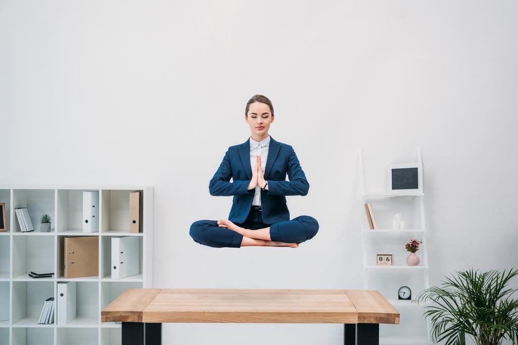jovem empresária com olhos fechados meditando enquanto levita no local de trabalho
  - Foto, Imagem