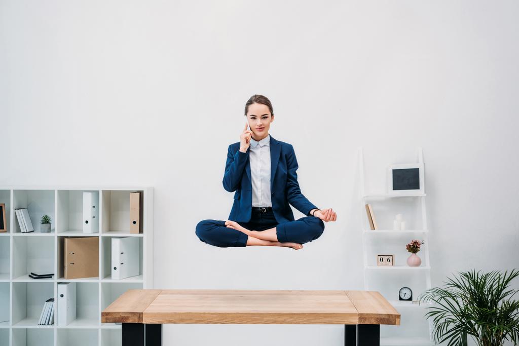 business woman talking by smartphone and looking at camera while levitating in office
 - Фото, изображение