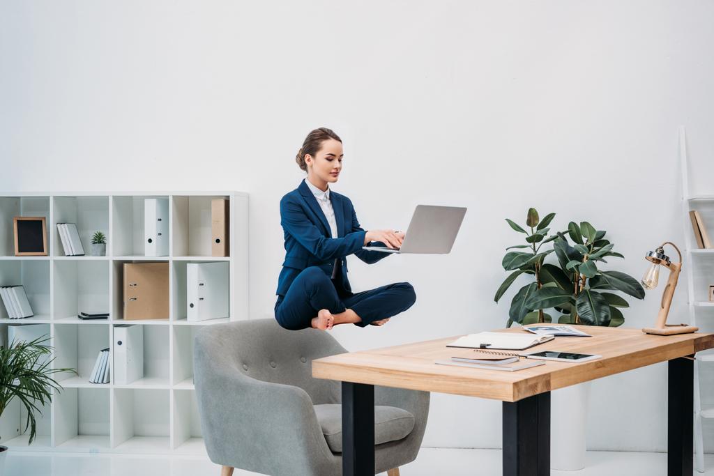 businesswoman using laptop while levitating at workplace  - Photo, Image