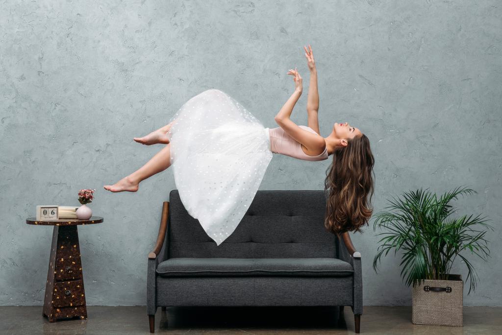 hermosa joven descalza mujer flotando sobre el sofá
  - Foto, Imagen