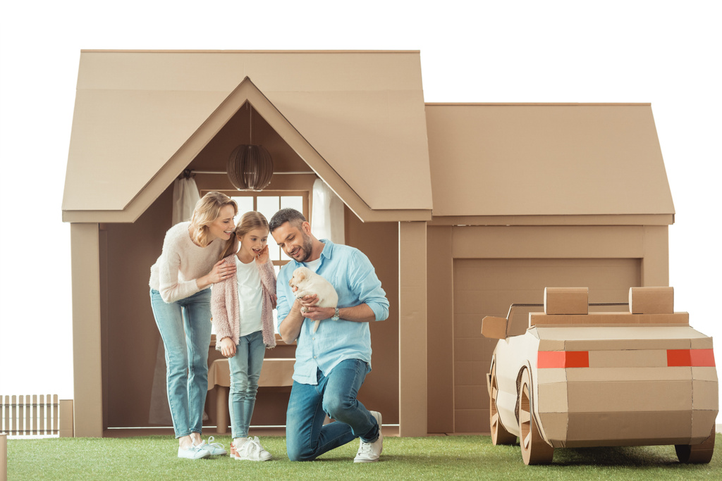 красивая семья с восхитительным щенком лабрадора перед картонным домиком, изолированным на белом
 - Фото, изображение