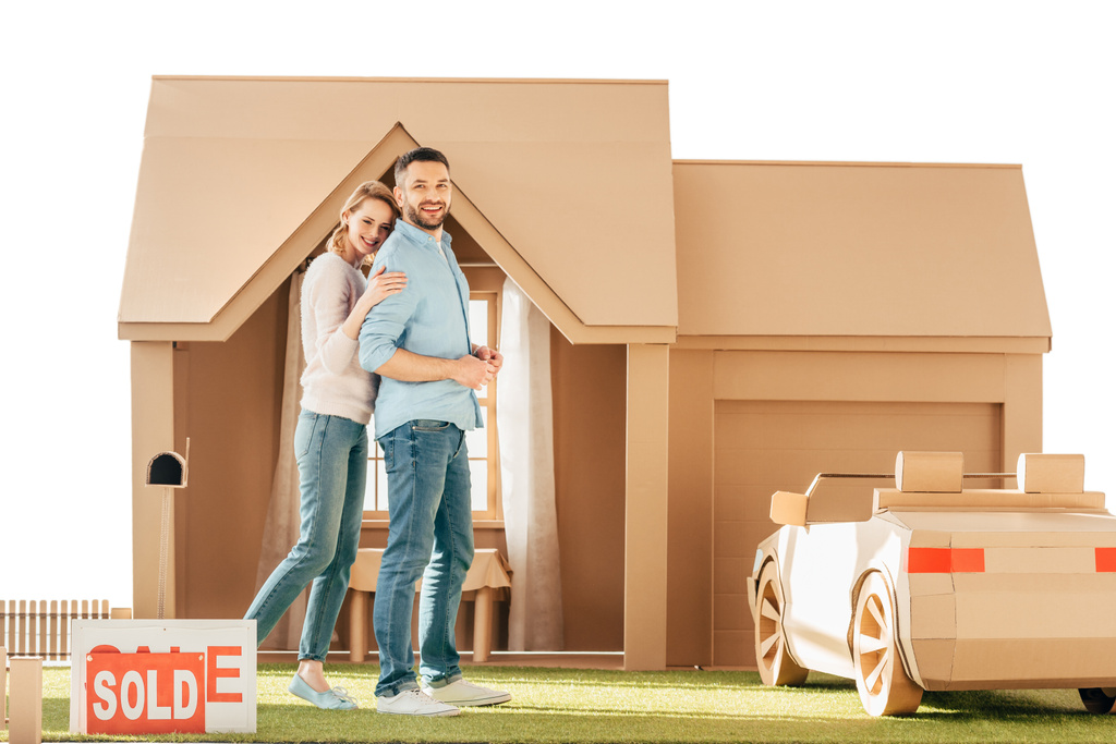 beautiful couple in front of their new cardboard house isolated on white - Photo, Image