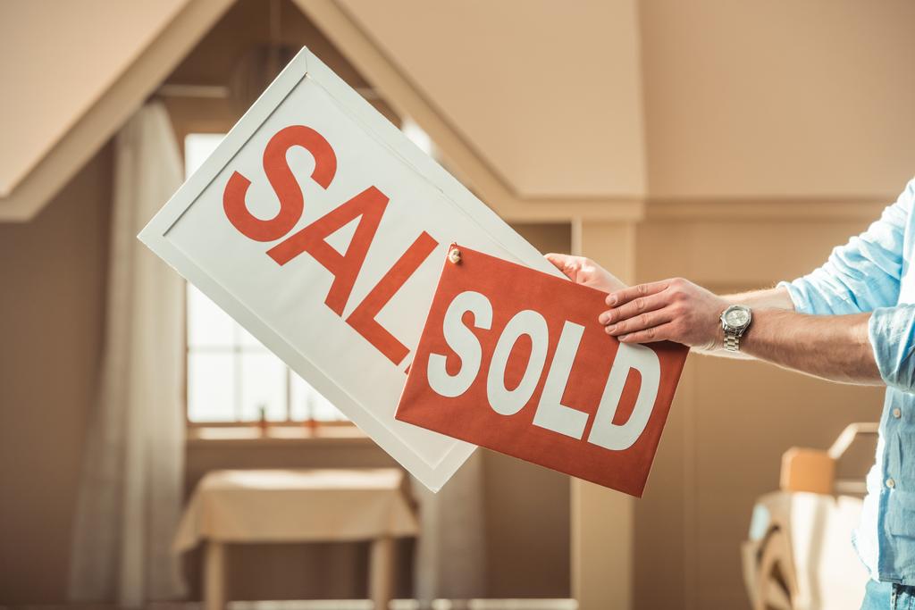 обрезанный снимок человека, проводящего продажу и продающего вывески перед картонным домом
 - Фото, изображение